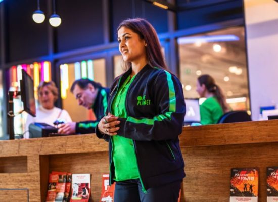 Bedrijfskleding One Planet Vest en Blouse Medewerker staat bij een balie