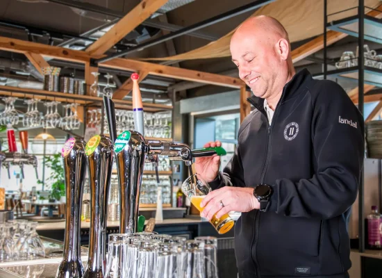Man schenkt een glas bier in achter de bar van een moderne horecalocatie van Landal.
