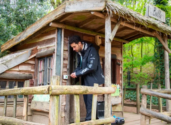 Technische medewerker van Landal voert werkzaamheden uit aan een houten accommodatie in een bosrijke omgeving.